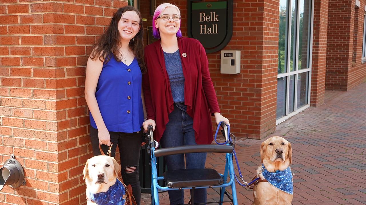 Photo of Kate and Zoe with their guide dogs Bernard and Mack in front of Belk Hall