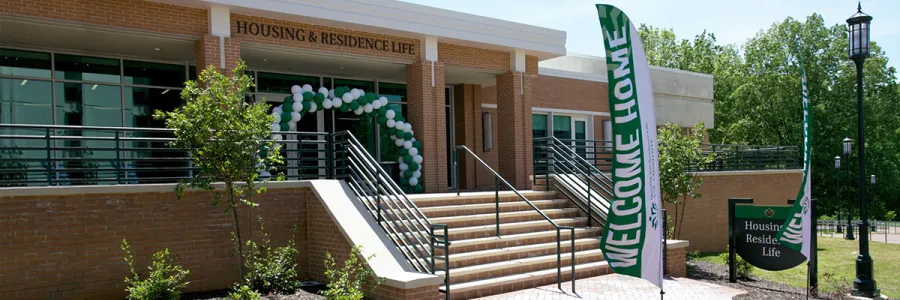 The Housing and Residence Life Building on campus with a green banner reading "Welcome Home"