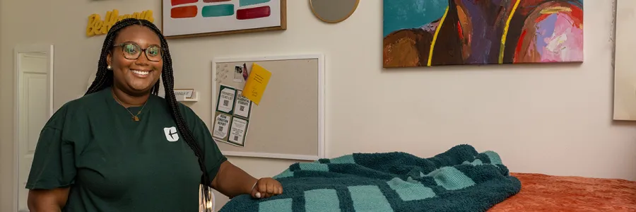 photo of a student standing next to their bed in their residence hall bedroom