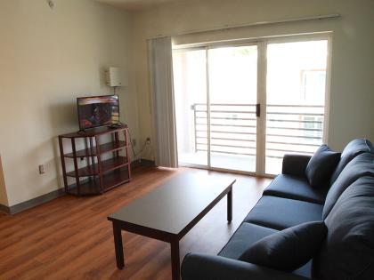 A lounge space next to a balcony sliding door consisting of a sofa with a coffee table in front of a television